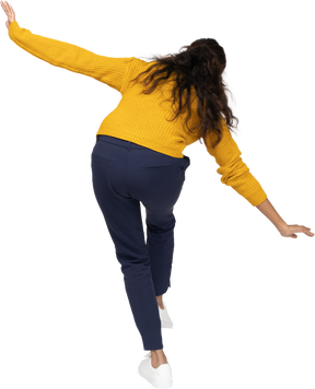 Rear view of a girl in casual clothes posing on one leg with outstretched arms